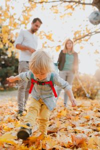 Copil la joacă printre frunze galbene de toamnă